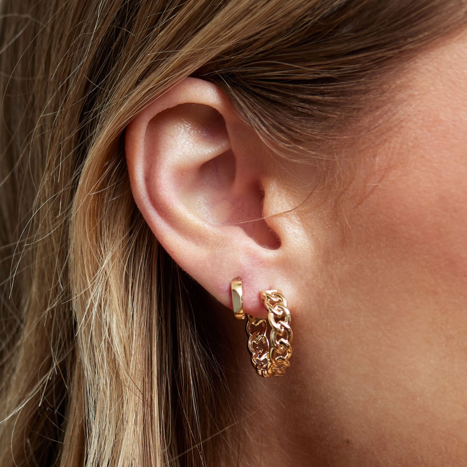 Close-up of a woman’s ear wearing multiple gold hoop earrings, including a pavé diamond hoop and smooth polished hoops in varying sizes. The earrings are crafted in yellow gold and styled with a cartilage cuff, showcasing a modern layered look.