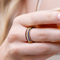 Gold ring with gemstones on a person's finger against a neutral background