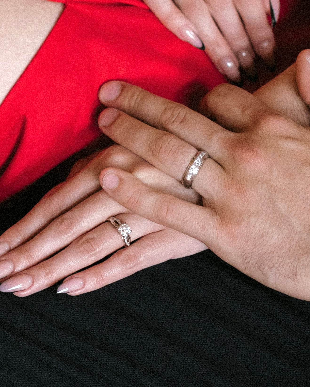 Close-up of two hands with diamond rings on a red and black background