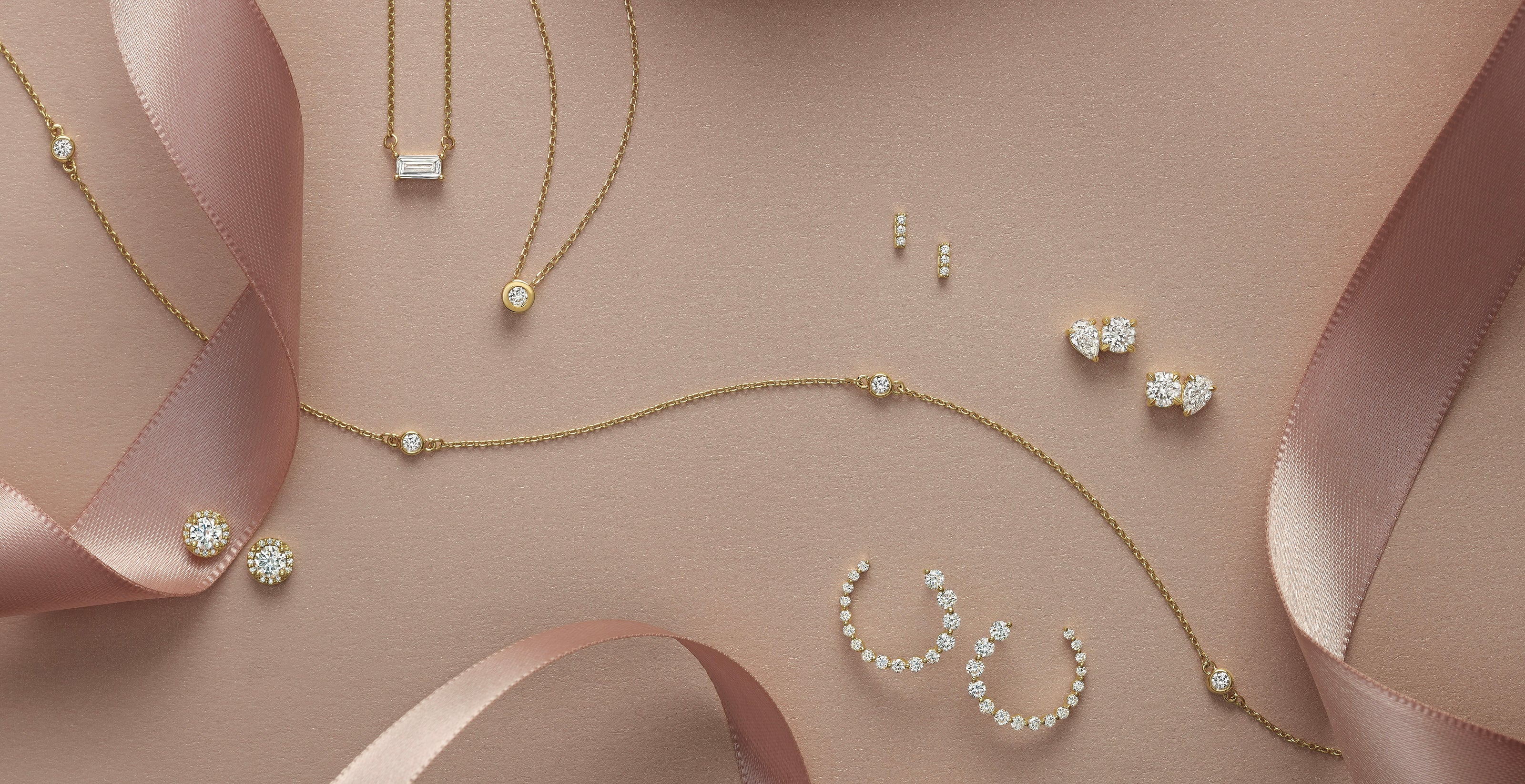 Gold jewelry set with necklaces, earrings, and rings on a soft pink background