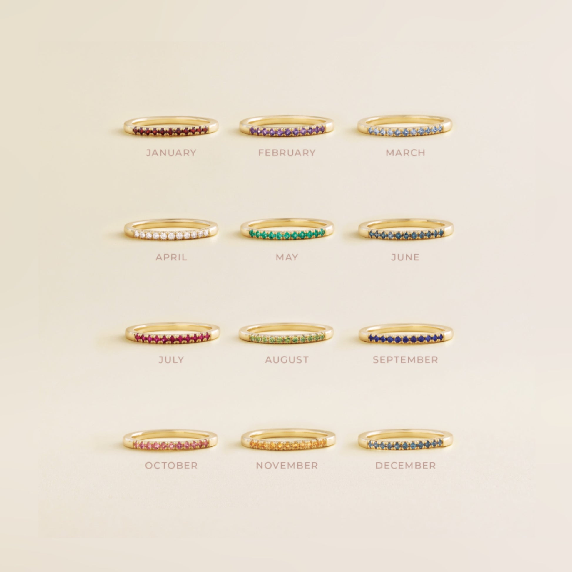 Set of gold rings with colored stones for each month, on a beige background.