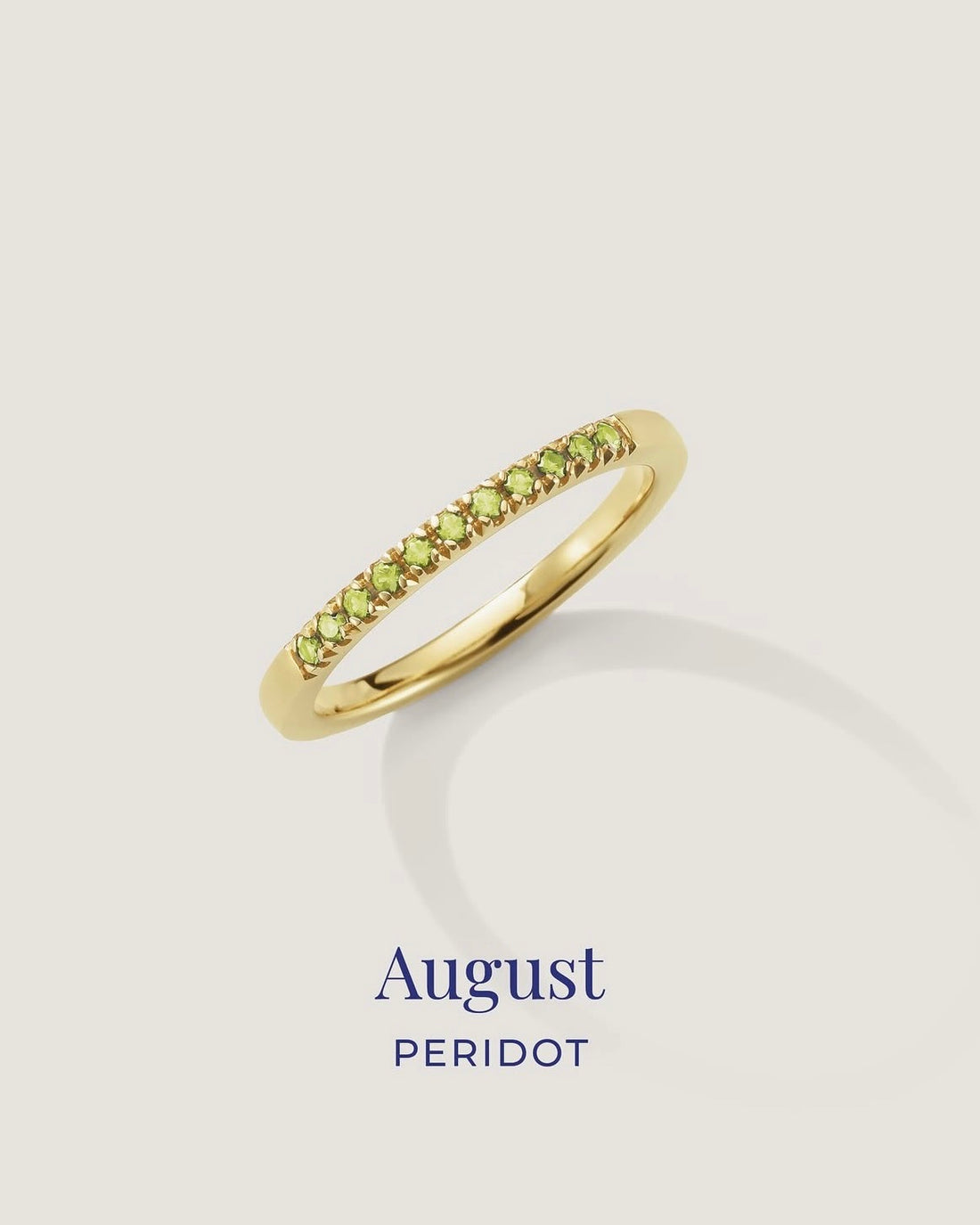 Gold ring with green gemstones on a light gray background, labeled 'August Peridot'.