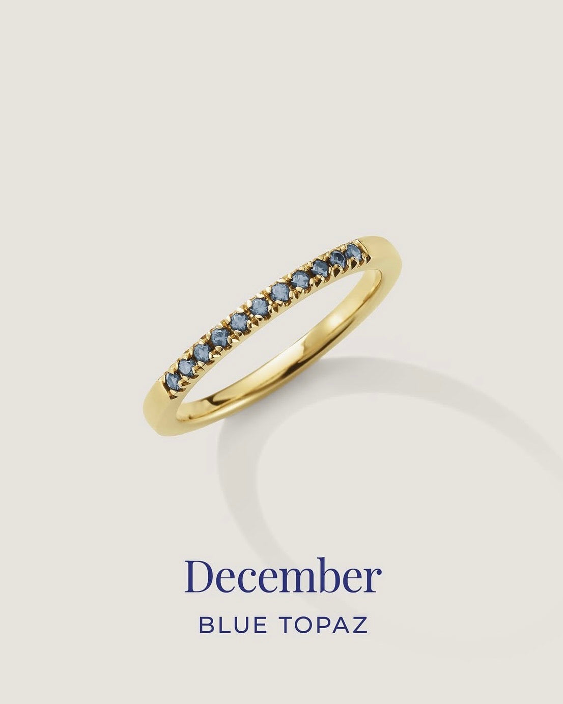 Gold ring with blue gemstones on a light gray background, labeled 'December Blue Topaz'.