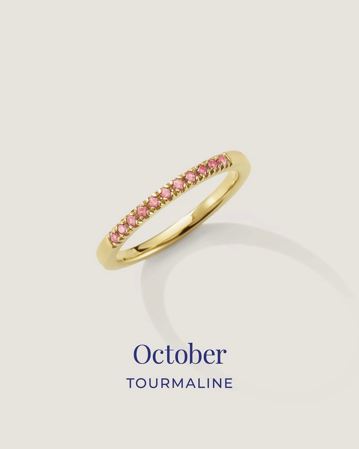 Gold ring with pink gemstones on a light gray background, labeled 'October Tourmaline'.